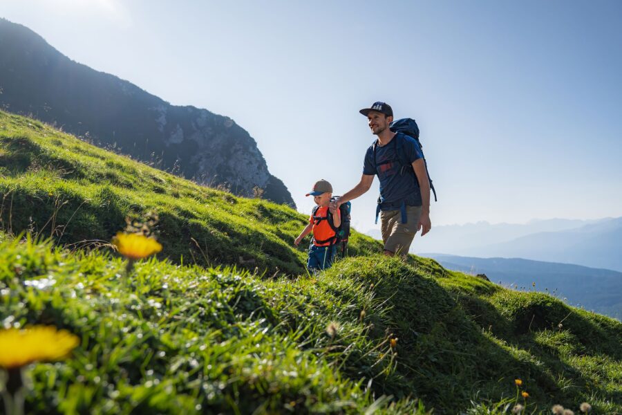 Vader en kind wandelen op een breed, vlak pad in Leutaschtal met bergen op de achtergrond.
